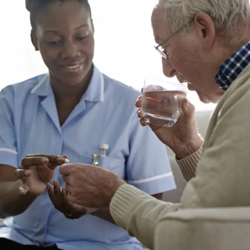 female-nurse-helping-senior-man-with-medication-at-home