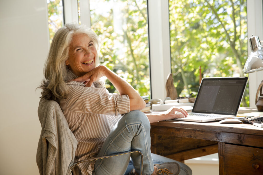 Portrait happy senior woman working from home at laptop